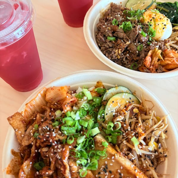 Two Korean bibimbap bowls with meat, vegetables, and eggs, alongside two red drinks.