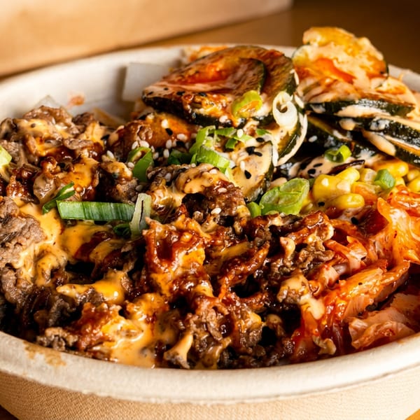 A close-up of a colorful Korean BBQ bowl with beef, kimchi, corn, zucchini, and sauces.