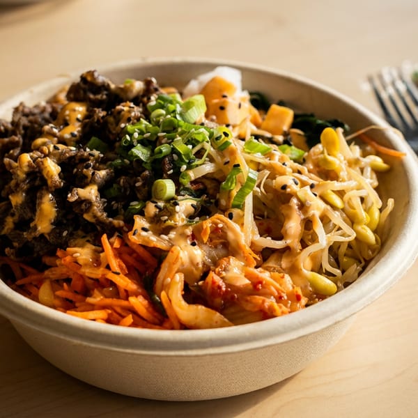 A colorful bibimbap bowl with beef, kimchi, bean sprouts, carrots, and green onions on a wooden table.